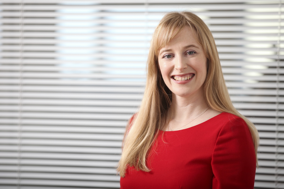 Kathryn stood in front of vertical blinds, she is smiling.