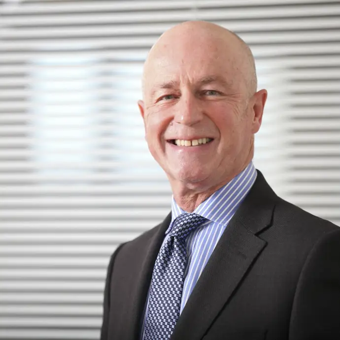Paul smiling, stood in front of a glass partition with vertical blinds.