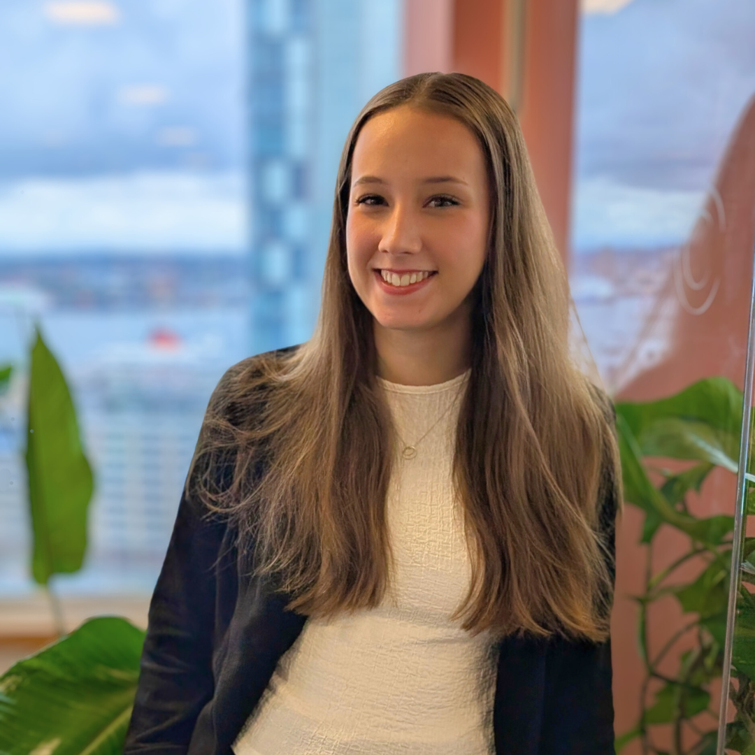 Molly smiling, stood next to a green plant in front of a window with a blush coloured pillar in the background.